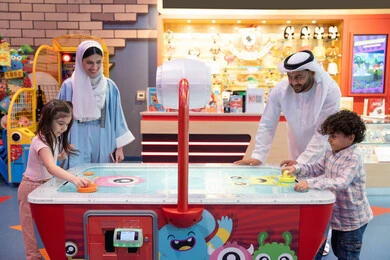 مراكز الالعاب الترفيهيه في الامارات، قضاء اوقات سعيده مع افراد الاسره ،منافسة مليئة بالتحدي والإثارة ، الأنشطة الرياضية الممتعة،  طاولة مضيئة بألوان زاهية ،  أجواء مليئة بالمرح والسرور، عائله عربية خليجية إماراتية  تستمتع بلعب الهوكي الهوائي فى مدينه الالعاب