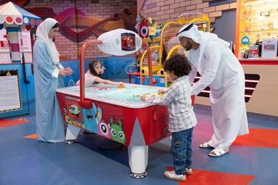 طاولة مضيئة بألوان زاهية ، الأنشطة الرياضية الممتعة، منافسة مليئة بالتحدي والإثارة ،مراكز الالعاب الترفيهيه في الامارات، قضاء اوقات سعيده مع افراد الاسره ، أجواء مليئة بالمرح والسرور، عائله عربية خليجية إماراتية  تستمتع بلعب الهوكي الهوائي فى مدينه الالعاب