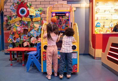 Fun sports activities, challenging and exciting competition, family interaction, and an atmosphere full of fun and enthusiasm. An Emirati Gulf Arab boy, wearing casual clothes, shares fun moments with his sister playing electronic basketball at an entertainment center in the UAE.