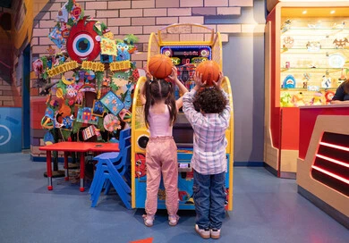 A challenging and exciting competition, fun sports activities, family interaction, and an atmosphere full of fun and enthusiasm. An Emirati Gulf Arab boy, wearing casual clothes, shares fun moments with his sister playing electronic basketball at an entertainment center in the UAE.