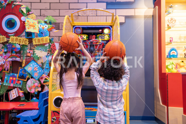 Family interaction, challenging and exciting competition, fun sports activities, and an atmosphere full of fun and enthusiasm. An Emirati Gulf Arab boy, wearing casual clothes, shares fun moments with his sister playing electronic basketball at an entertainment center in the UAE.