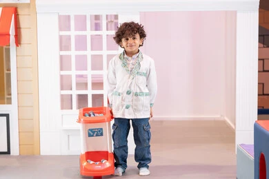 تقمص الأدوار المهنية، تجربة ممتعة تحاكي عمل الأطباء، مفهوم التعليم عن طريق اللعب ،ولد عربي خليجي اماراتي يرتدي معطف طبي ، يلعب بعربة ألعاب طبية في أحد المراكز الترفيهية للأطفال، ايماءات البراءة والمرح، تعزيز قيم المسؤولية والاهتمام بالآخرين ، تنمية المهارات الذهنية والخيالية لدى الأطفال