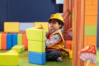 ولد عربي خليجي إماراتي يرتدي الخوذة وسترة الحماية يقوم بتركيب المكعبات ، مراكز الالعاب الترفيهيه في الامارات، رعاية وتطوير مهارات الأطفال، قضاء أوقات ممتعة باللعب والتركيز، الابداع وتنمية المهارات الذهنية والفكرية