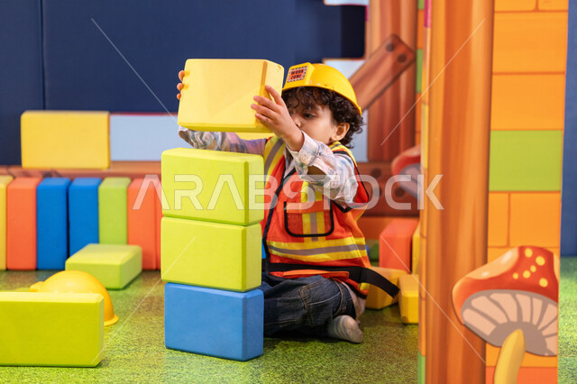 مراكز الالعاب الترفيهيه في الامارات، رعاية وتطوير مهارات الأطفال، قضاء أوقات ممتعة باللعب والتركيز، الابداع وتنمية المهارات الذهنية والفكرية،ولد عربي خليجي إماراتي يرتدي الخوذة وسترة الحماية يقوم بتركيب المكعبات