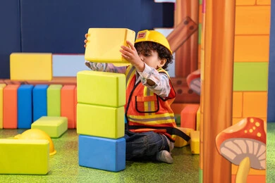 مراكز الالعاب الترفيهيه في الامارات، رعاية وتطوير مهارات الأطفال، قضاء أوقات ممتعة باللعب والتركيز، الابداع وتنمية المهارات الذهنية والفكرية،ولد عربي خليجي إماراتي يرتدي الخوذة وسترة الحماية يقوم بتركيب المكعبات