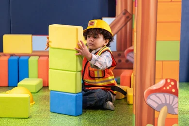 Caring for and developing children's skills, spending fun times playing and focusing, creativity and developing mental and intellectual skills, an Emirati Gulf Arab boy wearing a helmet and a protective vest assembling cubes, entertainment game centers in the Emirates