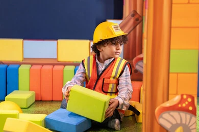 Spending fun times playing, focusing, creativity and developing mental and intellectual skills. An Emirati Gulf Arab boy wearing a helmet and a protective vest assembling blocks. Entertainment play centers in the Emirates, caring for and developing children's skills.