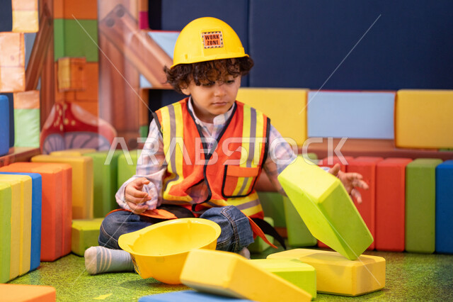 مراكز الالعاب الترفيهيه في الامارات، قضاء أوقات ممتعة باللعب والتركيز،  رعاية وتطوير مهارات الأطفال، تعزيز المهارات الذهنية والفكرية، ولد عربي خليجي إماراتي يرتدي الخوذة وسترة الحماية يقوم بتركيب المكعبات