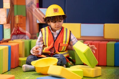 Entertainment play centers in the Emirates, spending fun times playing and focusing, caring for and developing children's skills, enhancing mental and intellectual skills, an Emirati Gulf Arab boy wearing a helmet and a protective vest assembling blocks