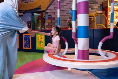 تعابير الحب والاحتواء،  تنمية مهارات الأطفال، قضاء اوقات سعيده فى مدينه الالعاب، أجواء مليئة بالمرح والسعادة ، مفهوم التفاعل الأسري ، سيدة عربية خليجية إماراتية ترتدي العباءة والحجاب تشارك ابنتها لحظات ممتعة فى لعبة المراجيح الدوارة ذات الألوان الزاهية، مركز ألعاب ترفيهي في الإمارات، الاهتمام ودعم الابناء