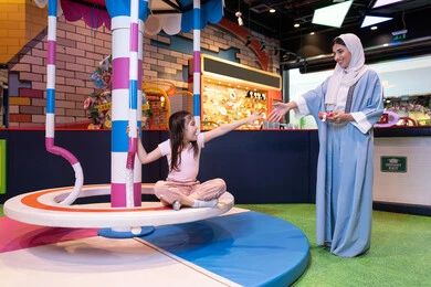 الاهتمام ودعم الابناء ،تنمية مهارات الأطفال، مفهوم التفاعل الأسري ، ايماءات الحب والاحتواء،مركز ألعاب ترفيهي في الإمارات، أجواء مليئة بالمرح والسعادة ، سيدة عربية خليجية إماراتية ترتدي العباءة والحجاب تشارك ابنتها لحظات ممتعة فى لعبة المراجيح الدوارة ذات الألوان الزاهية