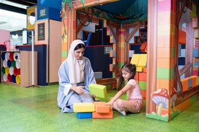 An Emirati Gulf Arab girl wearing a helmet and a safety vest, a Saudi Gulf Arab mother assembling blocks with her daughter, entertainment centers in the Emirates, spending fun times playing and concentrating, caring for and supporting children, caring for and developing children's skills, enhancing mental and intellectual skills