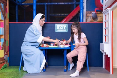 شغف البنات في المطبخ والطهي،  دعم وتنمية مهارات الطبخ عند الأطفال، الاستمتاع في اللعب في مركز الالعاب الترفيهيه، فتاة عربية خليجية إماراتية ترتدي الزي الكاجوال تقف أمام طاولة عليها مجموعة من ادوات الطبخ برفقه والدتها ، مهن ووظائف مستقبلية