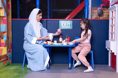 مهن ووظائف مستقبلية ، الاهتمام ودعم الابناء، الاستمتاع في اللعب في مركز الالعاب الترفيهيه،شغف البنات في المطبخ والطهي،  دعم وتنمية مهارات الطبخ عند الأطفال، فتاة عربية خليجية إماراتية ترتدي الزي الكاجوال تقف أمام طاولة عليها مجموعة من ادوات الطبخ برفقه والدتها