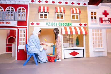 Enhancing children's skills, teaching children to shop for fresh produce from the grocery store, having fun at the amusement center, expressions of pleasure and happiness, a veiled Emirati Gulf Arab woman sharing fun moments with her daughter, a Saudi Gulf Arab girl wearing casual clothes