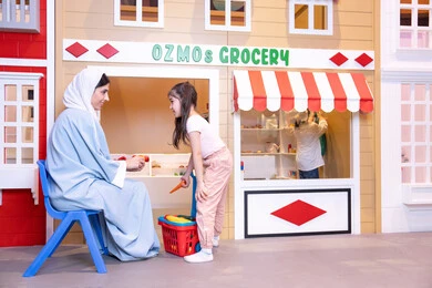 Teaching children to shop for fresh produce from the grocery store, having fun at the amusement park, expressions of joy and happiness, a veiled Emirati Gulf Arab woman sharing fun moments with her daughter, supporting and developing children's skills, a Saudi Gulf Arab girl wearing casual clothes