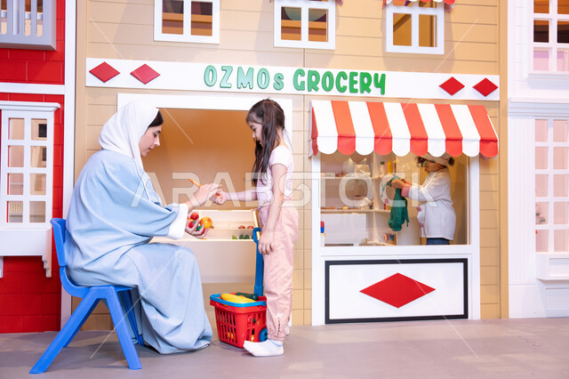 Having fun at the amusement park, teaching children to shop for fresh produce from the grocery store, expressions of joy and happiness, a veiled Emirati Gulf Arab woman sharing fun moments with her daughter, supporting and developing children's skills, a Saudi Gulf Arab girl wearing casual clothes