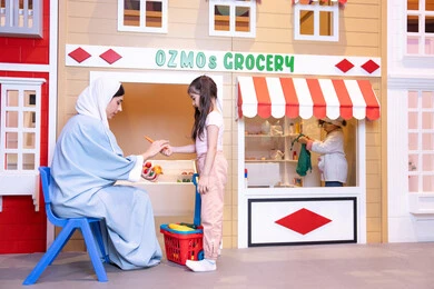 Having fun at the amusement park, teaching children to shop for fresh produce from the grocery store, expressions of joy and happiness, a veiled Emirati Gulf Arab woman sharing fun moments with her daughter, supporting and developing children's skills, a Saudi Gulf Arab girl wearing casual clothes