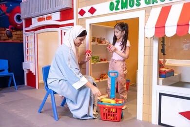 A Saudi Arabian Gulf girl wearing casual clothes, having a good time at the amusement center, teaching her children to shop for fresh produce from the grocery store, supporting and developing children's skills, a veiled Emirati Arabian Gulf woman sharing fun moments with her daughter, expressions of pleasure and happiness