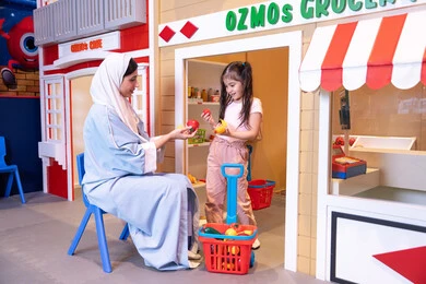 Teaching children to shop for fresh produce from the grocery store, having fun at the amusement park, a Saudi Arabian Gulf girl wearing casual clothes, supporting and developing children's skills, a veiled Emirati Arabian Gulf woman sharing fun moments with her daughter, expressions of pleasure and happiness