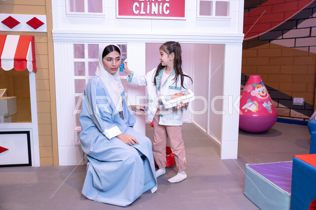 Medicine and healthcare, having fun at an amusement park, the concept of learning through play, introducing children to future careers, an Emirati mother wearing an abaya playing with her daughter, a Saudi Arabian Gulf girl wearing a medical uniform treating her mother