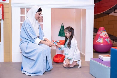 أم إماراتية ترتدي عباءة تقوم باللعب مع ابنتها،  فتاة عربية خليجية سعودية ترتدي الزي الطبي تقوم بمعالجه والدتها ،وسائل ايضاح تعليميه ممتعه ، مفهوم التعليم عن طريق اللعب،الاستمتاع في مركز الالعاب الترفيهي، الطب والرعاية الصحية،  تعريف الأطفال على المهن المستقبلية