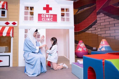 فتاة عربية خليجية سعودية ترتدي الزي الطبي تقوم بمعالجه والدتها ،وسائل ايضاح تعليميه ممتعه ، مفهوم التعليم عن طريق اللعب،الاستمتاع في مركز الالعاب الترفيهي، الطب والرعاية الصحية،  تعريف الأطفال على المهن المستقبلية، أم إماراتية ترتدي عباءة تقوم باللعب مع ابنتها