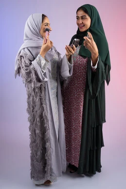 Elegant women's salon, portrait of two Emirati Gulf Arab women wearing hijab and abaya, one of them holding blush in her hand, and the other spraying perfume, marketing for women's beauty products and perfumes, the concept of femininity and interest in outward appearance, makeup and makeup tutorial, two Saudi friends using modern women's cosmetics, colorful background
