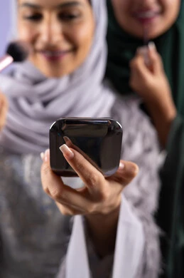 مفهوم الانوثه والاهتمام بالمظهر الخارجي, التسويق لمنتجات التجميل, مكياج وميكاب تتوريال, صديقتان سعوديتان تقومان باستخدام أدوات تجميل نسائيه عصريه، بورتريه مقرب لسيدتان عربيتان خليجيتان اماراتيان ترتديان الحجاب والعباءة احداهما تحمل بيدها مستحضرات توريد الخدود, صالون نسائي راقي, خلفيه ملونه