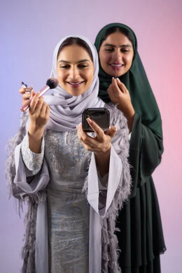 مكياج وميكاب تتوريال, صديقتان سعوديتان تقومان باستخدام أدوات تجميل نسائيه عصريه، التسويق لمنتجات التجميل, بورتريه لسيدتان عربيتان خليجيتان اماراتيان ترتديان الحجاب والعباءة احداهما تحمل بيدها مستحضرات توريد الخدود, مفهوم الانوثه والاهتمام بالمظهر الخارجي, صالون نسائي راقي, خلفيه ملونه