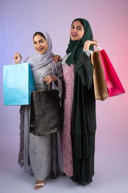 بورتريه مقرب لسيدتان عربيتان خليجيتان اماراتيان ترتديان الحجاب والعباءة تحملان بايديهم أكياس كرتون ملونه، تعابير وايماءات السرور والسعادة ،  الاستفادة من العروض والخصومات،  صديقتان سعوديتان تقومان بالتسوق وشراء المستلزمات,الأثر الايجابي للتسوق على نفسية المرأة، خلفية ملونه