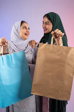 Close-up portrait of two Emirati Gulf Arab women wearing hijab and abaya holding colorful cardboard bags, positive impact of shopping on women's psychology, wearing sunglasses to protect from the sun's rays, taking advantage of offers and discounts, two Saudi friends shopping and buying necessities, expressions and gestures of pleasure and happiness, colorful background