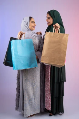 الأثر الايجابي للتسوق على نفسية المرأة، ارتداء النظارات الشمسيه للحمايه من اشعه الشمس، الاستفادة من العروض والخصومات،  صديقتان سعوديتان تقومان بالتسوق وشراء المستلزمات,  تعابير وايماءات السرور والسعادة ، بورتريه مقرب لسيدتان عربيتان خليجيتان اماراتيان ترتديان الحجاب والعباءة تحملان بايديهم أكياس كرتون ملونه،خلفية ملونه
