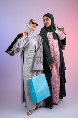 بورتريه  لسيدتان عربيتان خليجيتان اماراتيان ترتديان الحجاب والعباءة تحملان بايديهم أكياس كرتون ملونه، صديقتان سعوديتان تقومان بالتسوق وشراء المستلزمات, ارتداء النظارات الشمسيه للحمايه من اشعه الشمس، الاستفادة من العروض والخصومات، تعابير وايماءات السرور والسعادة ،  خلفية ملونه