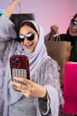 التسوق الالكتروني الآمن عبر الانترنت، صديقتان سعوديتان تقومان بالتسوق وشراء المستلزمات, بورتريه لسيدتان عربيتان خليجيتان اماراتيان ترتديان الحجاب والعباءة تحملان بايديهم أكياس كرتون ملونه، احداهما تقوم بالتقاط صور سيلفي، مشاركة اليوميات عبر وسائل التواصل الاجتماعي، خلفية ملونة