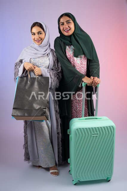الاهتمام بالأناقة والمظهر الخارجي، الاستعداد لرحلة سياحية ،قضاء أوقات ممتعة في التسوق برفقة الأصدقاء،امراه سعوديه تحمل بيدها اكياس التسوق بايماءات البهجه والسعادة،  بورتريه لسيدتان عربيتان خليجيتان اماراتيان ترتديان الحجاب والعباءة مبتسمتان ، تنظران الى مكان ما بإيماءات السرور ، مفهوم الأنوثة والنعومة، خلفية ملونه