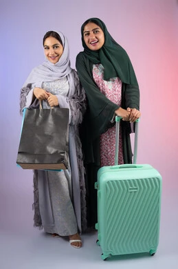 الاهتمام بالأناقة والمظهر الخارجي، الاستعداد لرحلة سياحية ،قضاء أوقات ممتعة في التسوق برفقة الأصدقاء،امراه سعوديه تحمل بيدها اكياس التسوق بايماءات البهجه والسعادة،  بورتريه لسيدتان عربيتان خليجيتان اماراتيان ترتديان الحجاب والعباءة مبتسمتان ، تنظران الى مكان ما بإيماءات السرور ، مفهوم الأنوثة والنعومة، خلفية ملونه