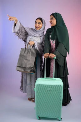قضاء أوقات ممتعة في التسوق برفقة الأصدقاء،امراه سعوديه تحمل بيدها اكياس التسوق وتشير الى شئ ما بايماءات البهجه والسعادة، الاستعداد لرحلة سياحية ، بورتريه لسيدتان عربيتان خليجيتان اماراتيان ترتديان الحجاب والعباءة مبتسمتان ، تنظران الى مكان ما بإيماءات السرور ، مفهوم الأنوثة والنعومة، الاهتمام بالأناقة والمظهر الخارجي،  خلفية ملونه