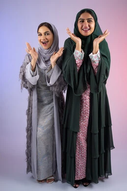 بورتريه لسيدتان عربيتان خليجيتان اماراتيان ترتديان الحجاب والعباءة مبتسمتان ، تنظران بإيماءات الثقة بالنفس والفرح، مفهوم الأنوثة والنعومة، صديقتان سعوديتان تضعان ايديهم تحت وجههم بتعابير البهجه ، الاهتمام بالأناقة والمظهر الخارجي، ايماءات السرور والسعادة،  خلفية ملونه
