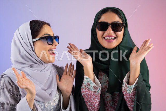 Wearing sunglasses to protect from the sun's rays, close-up portrait of two Arab Gulf Emirati women wearing hijab and abaya, smiling, looking with gestures of self-confidence and joy, the concept of femininity and softness, two Saudi friends putting their hands under their faces with expressions of joy, interest in elegance and outward appearance, gestures of pleasure and happiness, colorful background