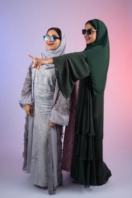 الاشاره الى شئ ما بايماءات البهجه والسعادة،  ارتداء النظارات الشمسيه للحمايه من اشعه الشمس ،بورتريه لسيدتان عربيتان خليجيتان اماراتيان ترتديان الحجاب والعباءة مبتسمتان ، تنظران بإيماءات الثقة بالنفس والفرح، مفهوم الأنوثة والنعومة، صديقتان سعوديتان تضعان ايديهم تحت وجههم بتعابير السرور، الاهتمام بالأناقة والمظهر الخارجي،  خلفية ملونه
