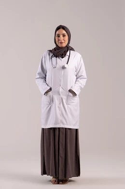 العمل في القطاع الصحي, تقديم المساعده الطبية للمرضى, شابة سعودية تقوم بالعمل في المراكز والمستشفيات, بورتريه لطبيبة عربية خليجية اماراتية ترتدي المعطف الطبي الأبيض وسماعة الفحص تنظر إلى الكاميرا بايماءات الثقة بالنفس, مفهوم الطب والرعاية الصحية, الجسم بالطول الكامل, خلفية بنية