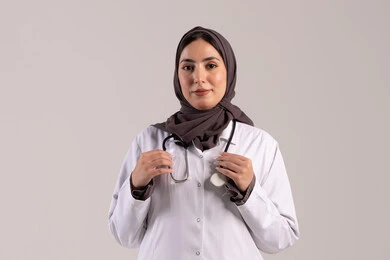 تقديم المساندة الطبية للمرضى, مهن ووظائف نسائية, , شابة سعودية تقوم بالعمل في المراكز والمستشفيات, بورتريه  لطبيبة عربية خليجية اماراتية ترتدي المعطف الطبي الأبيض وسماعة الفحص تنظر إلى الكاميرا بايماءات الثقة بالنفس, مفهوم الطب والرعاية الصحية, خلفية بنية