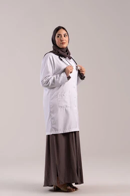 رعاية المرضى وتقديم المساعدة الصحية, مهن ووظائف نسائية, شابة سعودية تقوم بالعمل في المراكز والمستشفيات, بورتريه من الجانب لطبيبة عربية خليجية اماراتية ترتدي المعطف الطبي الأبيض وسماعة الفحص تنظر إلى الكاميرا بايماءات الثقة بالنفس, مفهوم الطب والرعاية الصحية, الجسم بالطول الكامل, خلفية بنية