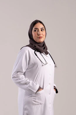 مساعدة المرضى بالخدمات الطبية, مهن ووظائف نسائية, شابة سعودية تقوم بالعمل في المراكز والمستشفيات, بورتريه من الجانب لطبيبة عربية خليجية اماراتية ترتدي المعطف الطبي الأبيض وسماعة الفحص تنظر إلى الكاميرا بايماءات الثقة بالنفس, مفهوم الطب والرعاية الصحية, خلفية بنية
