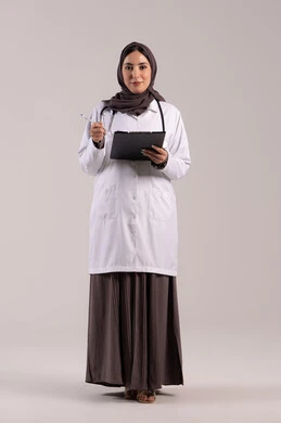 Monitoring and recording information and notes, working in centers and hospitals, medicine and healthcare, a portrait of an Arab Gulf Emirati female doctor wearing a white medical coat, wearing a stethoscope, holding a clipboard in her hand, a young Saudi woman providing medical assistance, brown background.