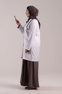 البرامج والتطبيقات الخاصة بالصحة, تقديم الخدمات والرعاية الصحية عبر الإنترنت، بورتريه من الجانب لطبيبة عربيه خليجيه امارتية ترتدي المعطف الطبي و السماعه تقوم باستخدام الهاتف المحمول، استخدام الأجهزة التقنية الحديثة ودمج التكنولوجيا مع الطب، الجسم بالطول الكامل, خلفية بنية