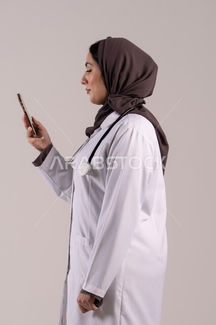 Health applications and programs, providing online health services and care, a side portrait of an Arab Gulf Emirati female doctor wearing a medical coat and stethoscope using a mobile phone, utilizing modern technological devices and integrating technology with medicine, brown background.
