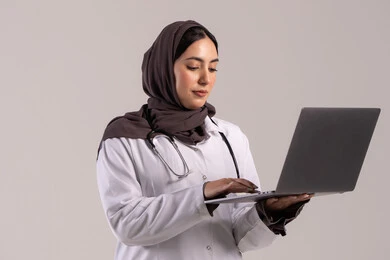 تسجيل وتدوين معلومات وملفات المرضى عبر الابتوب, دمج التقنية الحديثة في مجال العمل الطبي, بورترية لطبيبة عربية خليجية اماراتية ترتدي المعطف الطبي الأبيض وسماعة الفحص تحمل الحاسب المحمول, شابة سعودية تقوم بتقديم الخدمات العلاجية في المراكز الطبية والمستشفيات , خلفية بنيه