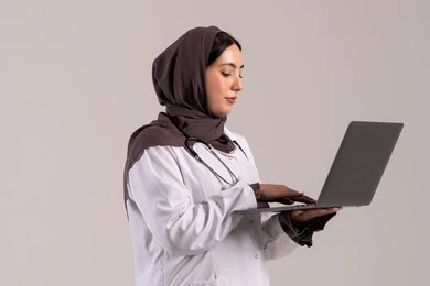 تسجيل وتدوين معلومات وملفات المرضى عبر الابتوب, دمج التقنية الحديثة في مجال العمل الطبي, بورترية لطبيبة عربية خليجية اماراتية ترتدي المعطف الطبي الأبيض وسماعة الفحص تحمل الحاسب المحمول, شابة سعودية تقوم بتقديم الخدمات العلاجية في المراكز الطبية والمستشفيات , خلفية بنيه